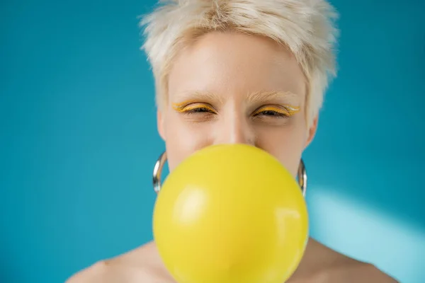 Blonde albino woman with bright eye liner blowing bubble gum on blue background — Stock Photo