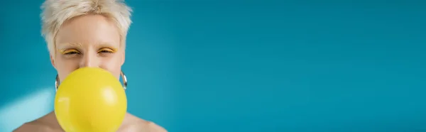 Blonde albino woman with bright eye liner blowing bubble gum on blue background, banner — Stock Photo