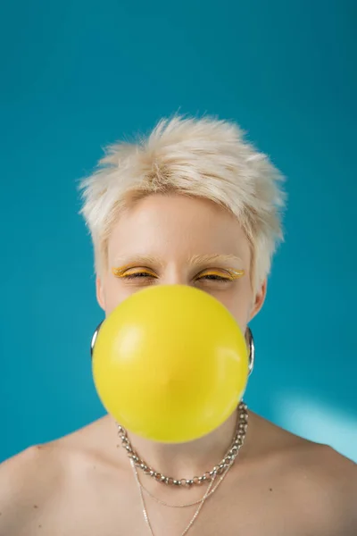 Femme albinos blonde avec doublure jaune soufflant gomme à bulles sur fond bleu — Photo de stock