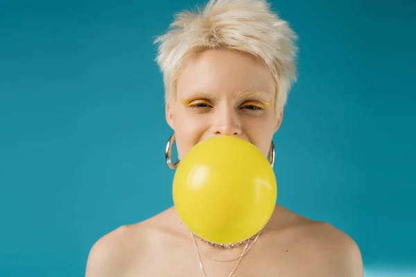 Blonde albino woman with bare shoulders blowing bubble gum on blue background — Stock Photo