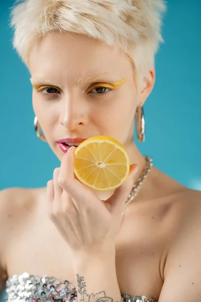 Blonde albino woman with bare shoulders holding lemon half on blue — Stock Photo