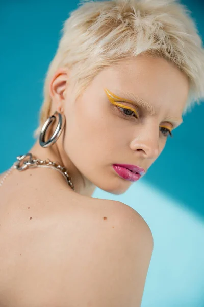 Modelo albino rubia con maquillaje de moda y hombro desnudo posando en azul - foto de stock