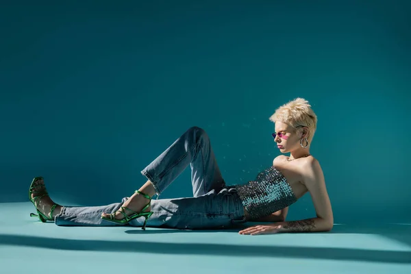 Seitenansicht des tätowierten Albino-Models in rosa Sonnenbrille posiert im trendigen Outfit auf blau — Stockfoto