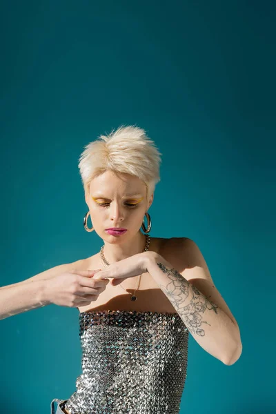 Татуированная модель альбиноса в модном наряде, позирующая на синем фоне — стоковое фото