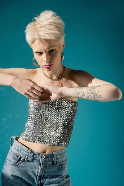 Tätowiertes Albino-Model im modischen Outfit blickt in die Kamera auf blauem Hintergrund — Stockfoto