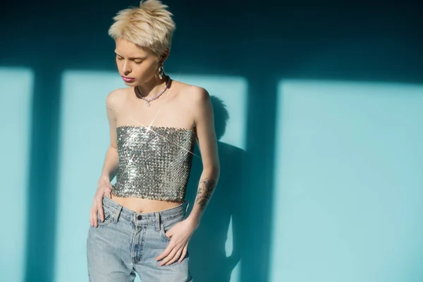Sunlight on albino woman in shiny top with sequins and jeans posing on blue background — Stock Photo