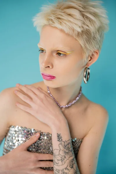 Blonde albino woman in shiny top with sequins posing on blue background — Stock Photo