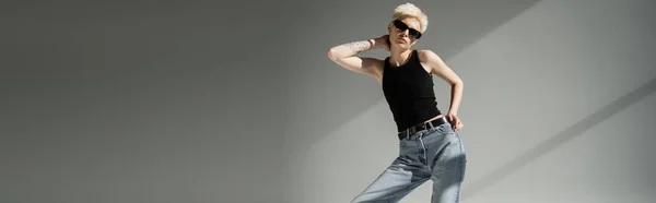 Tattooed woman in black sunglasses and tank top posing on grey background, banner — Stock Photo