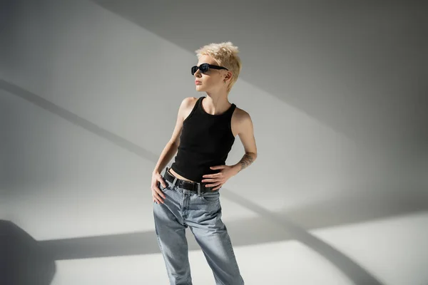Blondes und tätowiertes Model mit schwarzer Sonnenbrille posiert auf grauem Hintergrund — Stockfoto