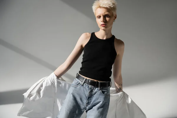 Femme albinos tatoué en débardeur noir et jeans décoller chemise blanche sur fond gris — Photo de stock