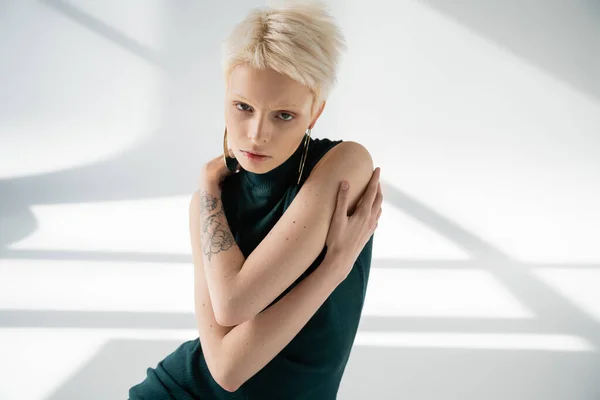 Giovane donna albina con tatuaggio a mano che si abbraccia su sfondo grigio con ombre — Foto stock