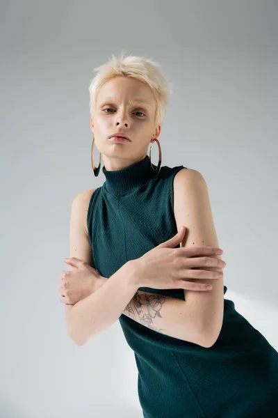 Татуированная альбиноса в обтягивающем платье обнимающая себя на сером фоне — стоковое фото