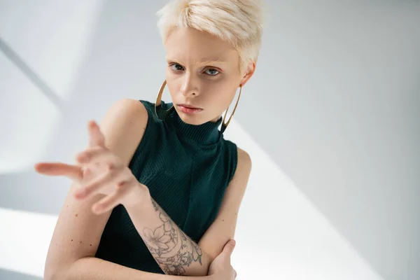 Tätowierte Albino-Frau mit heller Haut gestikuliert, während sie in die Kamera auf grauem Hintergrund blickt — Stockfoto