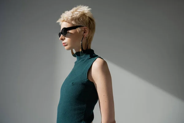 Blonde albino woman with fair-skin posing in stylish sunglasses and dress on grey background — Stock Photo