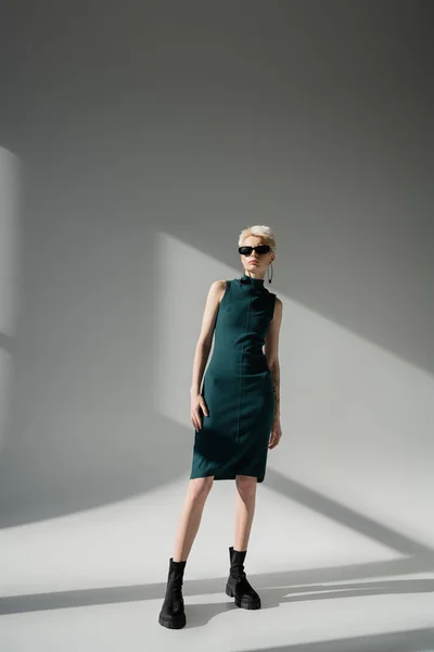 Volle Länge des stilvollen Modells mit Tätowierung posiert in Stiefeln und Kleid auf grauem Hintergrund — Stockfoto