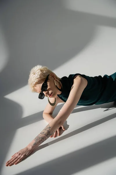 Modelo tatuado en gafas de sol y vestido posando sobre fondo gris con sombras — Stock Photo