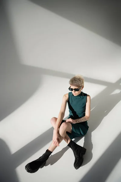 Overhead-Ansicht der tätowierten und blonden Frau mit Sonnenbrille sitzt auf grauem Hintergrund — Stockfoto