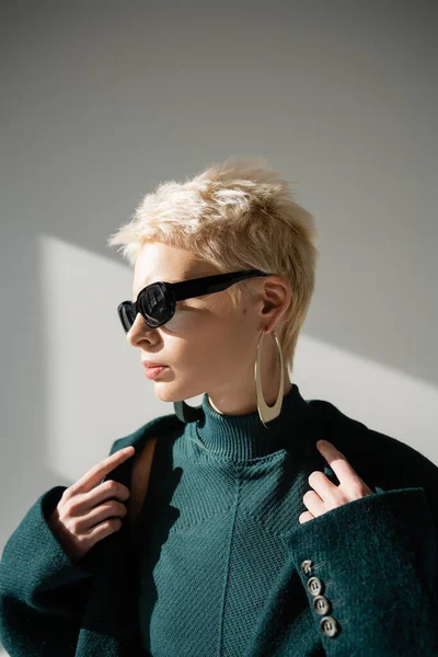 Model mit trendiger Sonnenbrille in grünem Kleid und Mantel auf grauem Hintergrund — Stockfoto