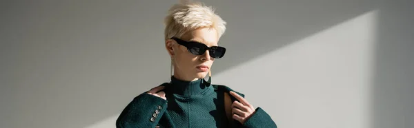 Блондинка модель в модних сонцезахисних окулярах в зеленому пальто на сірому фоні, банер — стокове фото