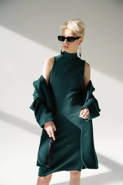 Blondine mit trendiger Sonnenbrille und grünem Mantel auf grauem Hintergrund — Stockfoto