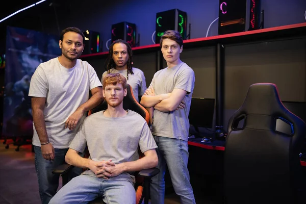 Multiethnic gamers in grey t-shirts looking at camera in cyber club — Stock Photo