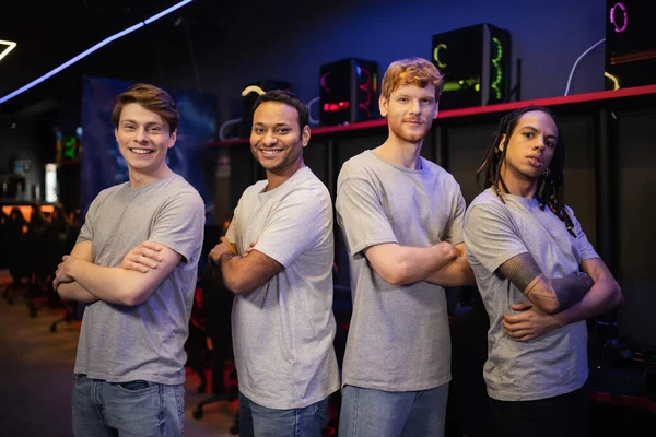 Cheerful interracial gamers crossing arms and looking at camera in gaming club — Stock Photo