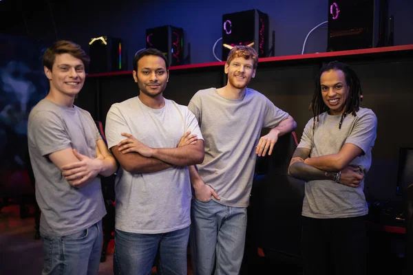 Cheerful interracial team crossing arms and looking at camera in gaming club — Stock Photo