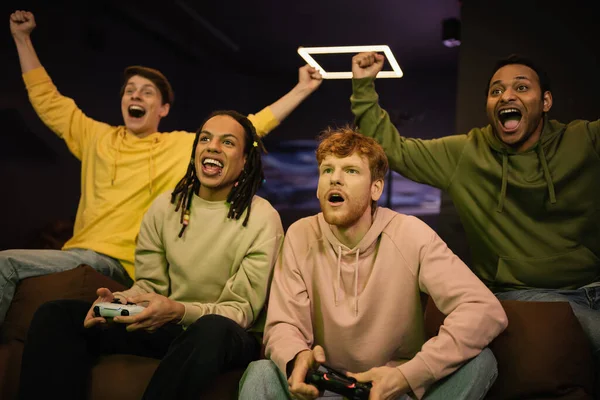 KYIV, UKRAINE - FEBRUARY 13, 2023: Excited interracial gamers playing video game near friends in cyber club — Stock Photo