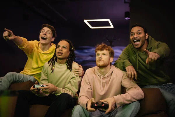 QUIIV, UCRÂNIA - FEVEREIRO 13, 2023: Homens multiétnicos jogando videogame perto de amigos alegres gesticulando no clube de jogos — Fotografia de Stock