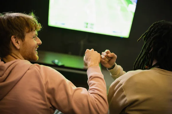 Sorrindo homem fazendo punho colisão com amigo multirracial no clube de jogos — Fotografia de Stock