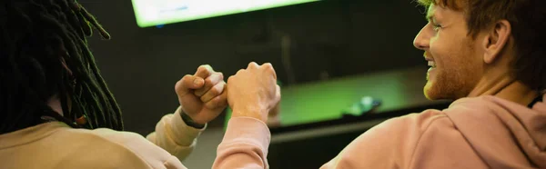 Улыбающийся молодой человек бьется кулаком с многонациональным другом в игорном клубе, баннер — стоковое фото