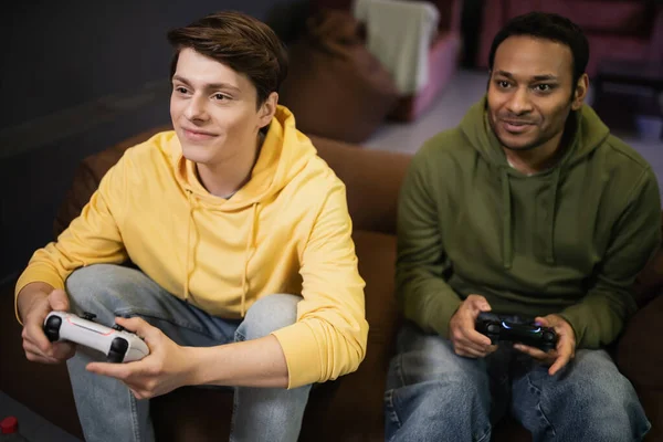 KYIV, UKRAINE - FEBRUARY 13, 2023: Pleased man playing video game with indian friend in gaming club — Stock Photo