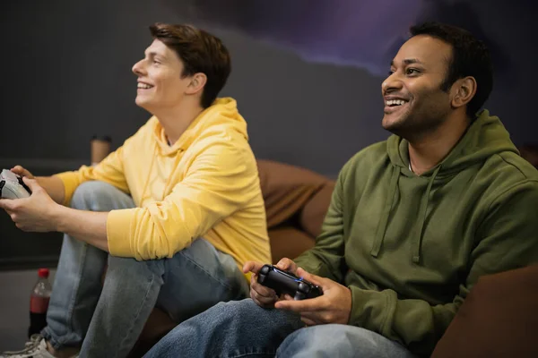 KYIV, UKRAINE - FEBRUARY 13, 2023: Smiling indian man playing video game near blurred friend in gaming club — Stock Photo