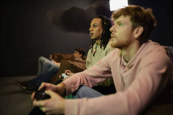 KYIV, UKRAINE - FEBRUARY 13, 2023: Multiracial man playing video game with blurred friend in gaming club — Stock Photo