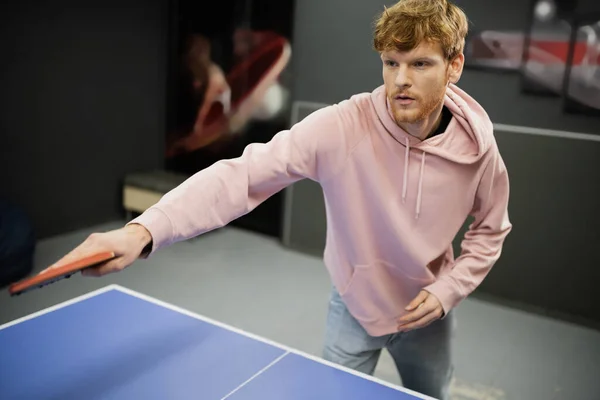 Homem ruivo em roupas casuais jogando tênis de mesa no clube de jogos — Fotografia de Stock