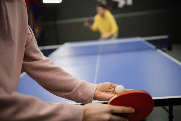 Vista recortada del hombre jugando al tenis de mesa con un amigo borroso en el club de juegos - foto de stock