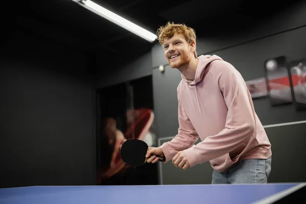 Веселый рыжий мужчина играет в настольный теннис в игорном клубе — стоковое фото
