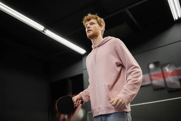 Low angle view of redhead man holding tennis racket in gaming club — Stock Photo