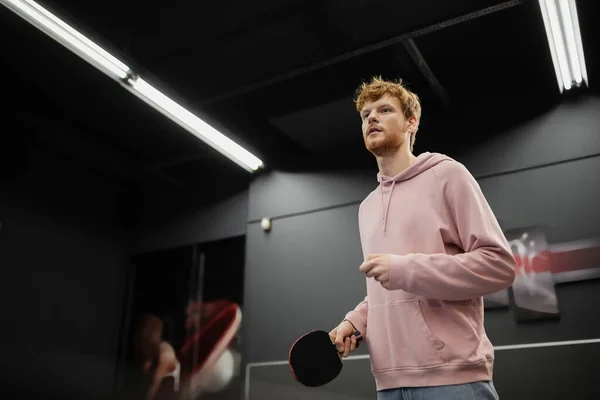 Jeune homme rousse avec raquette jouant au tennis de table dans un club de jeux — Photo de stock