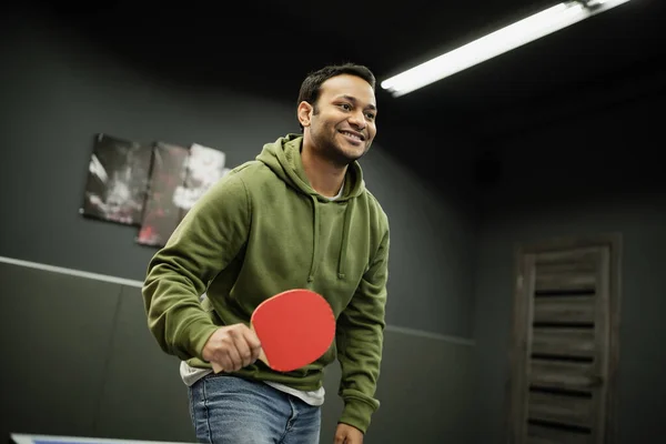 Hombre indio alegre con raqueta jugando al tenis de mesa en el club de juegos - foto de stock