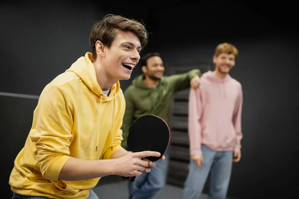 Веселый человек играет в настольный теннис рядом с размытыми друзьями в игорном клубе — стоковое фото