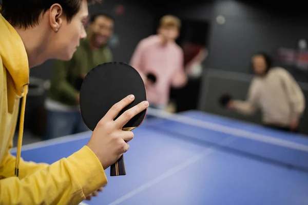 Jeune homme jouant au tennis de table avec des amis flous dans un club de jeu — Photo de stock