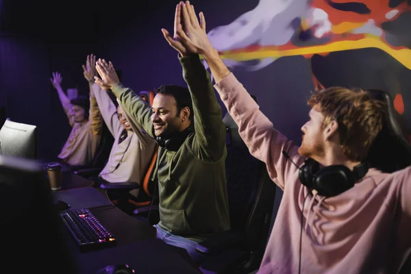 Cheerful indian player giving high five to friends near computers in cyber club — Stock Photo