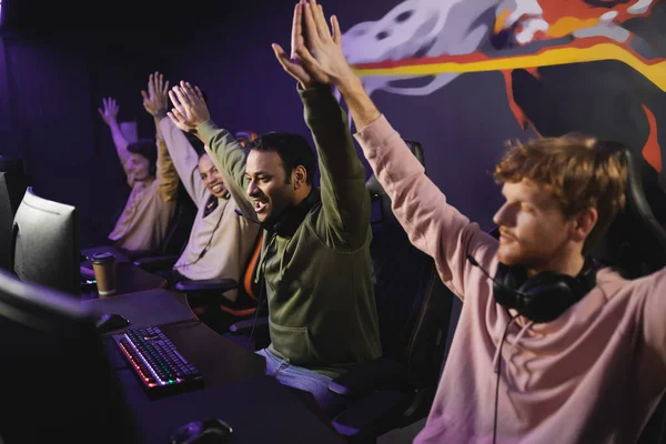 Excited indian man giving high five to friends near computers in gaming club — Stock Photo