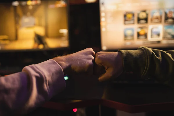 Обрізаний вигляд друзів, які роблять удари кулаком поблизу розмитих комп'ютерів в ігровому клубі — стокове фото