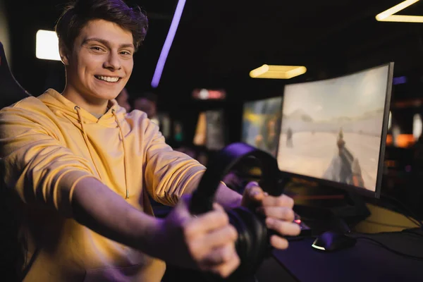 Alegre jugador celebración de auriculares cerca de la computadora borrosa en el club de juegos - foto de stock