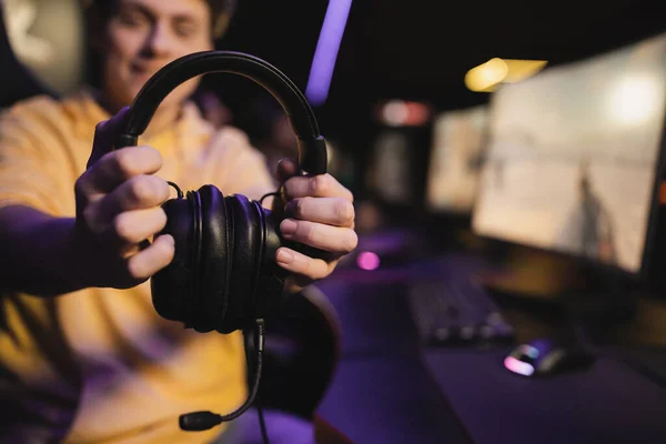 Homem desfocado segurando fones de ouvido com microfone no clube de jogos — Fotografia de Stock