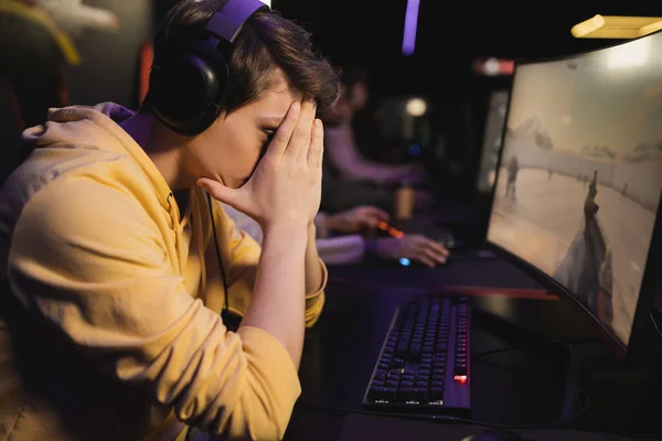 Triste joueur dans les écouteurs assis près de l'ordinateur dans le club de jeu — Photo de stock