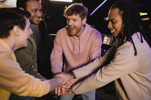 Cheerful multiethnic friends holding hands while spending time in gaming club — Stock Photo