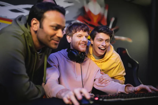 Улыбающийся человек играет в видеоигры рядом с многонациональными друзьями в игровом клубе — стоковое фото